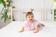 © Any Grant - cheerful baby girl six months crawling in a bright beautiful room on a white bed in pink clothes and smiling