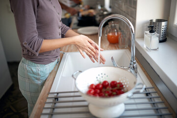 Wall Mural - A young girl washing cherry tomatoes for a salad. Vegetables, kitchen, home, food