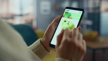 Wall Mural - Close Up on Hands Tapping on an Online Food Shopping App on a Horizontally Held Smartphone at Home Living Room. Feminine Hands Choosing Vegetables from a Mobile Phone Market Website On the Internet.
