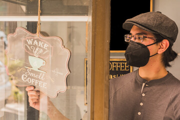 Waiter opening a local cafeteria, putting the open announcement so that customers can enter, wears a mask for sanitation  2