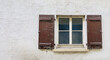 Alte Hauswand mit Quadratischem Sprossenfenster, rechts und links braune alte Holzläden und Fenstersims