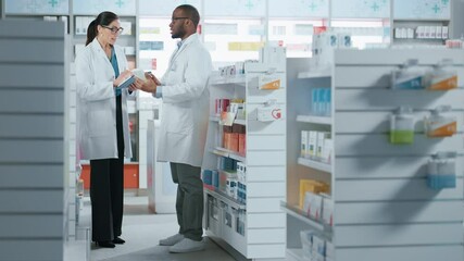 Wall Mural - Pharmacy: Black Male and Caucasian Female Pharmacists Use Digital Tablet Computer Talk about Medicine, Drugs, Vitamins, Supplements, Vaccine, Health Care Products. Medical Professionals in Drugstore