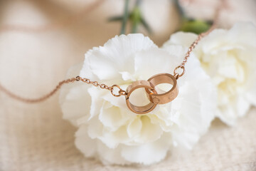 Closeup of a golden necklace with two ring pendants sitting against white carnations