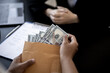© kamiphotos - Businesswoman pulls dollar bills out of brown envelopes, hand them over to business partners as a bribe, bribery is a corrupt and illegal act. The concept of bribery.