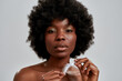 Portrait of beautiful african american young woman with afro hair looking at camera, holding white feather, posing isolated over gray background
