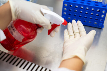 Young Asia scientist spray alcohol to his hand to sterilize and cleaning hand before doing research in the biohazard hood in the laboratory. Healthcare, research, education and Covid concept.