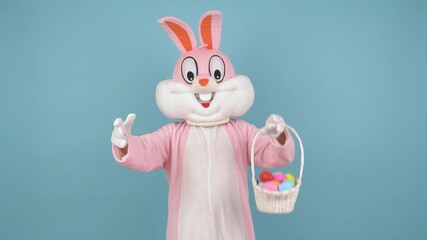 Wall Mural - Easter bunny or rabbit or hare holds basket of colored eggs, have fun, dancing, celebrate Happy easter. Easter rabbit isolated on blue background