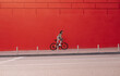 Sporty woman in casual clothes rides a bicycle on a city street on a background of a red wall and looks at the camera. Weekend cycling as a sport