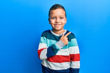 Wall Mural - Little kid boy wearing striped sweater smiling cheerful pointing with hand and finger up to the side