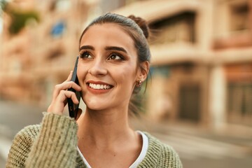 Wall Mural - Beautiful brunette woman smiling happy and confident outdoors at the city on a sunny day of autumn speaking on the phone