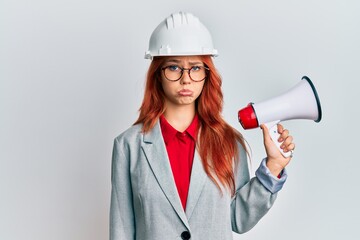 Sticker - Young redhead woman wearing architect hardhat and megaphone depressed and worry for distress, crying angry and afraid. sad expression.