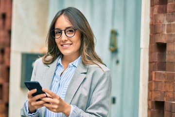 Wall Mural - Young hispanic businesswoman smiling happy using smartphone at the city.