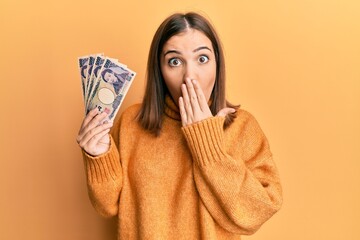 Poster - Young woman holding 5000 japanese yen banknotes covering mouth with hand, shocked and afraid for mistake. surprised expression