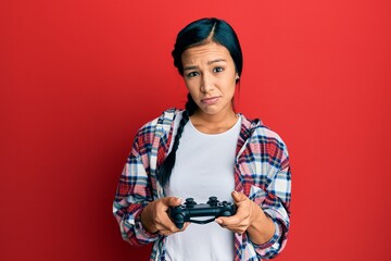 Sticker - Beautiful hispanic woman playing video game holding controller clueless and confused expression. doubt concept.