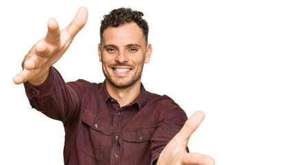 Sticker - Young hispanic man wearing casual clothes looking at the camera smiling with open arms for hug. cheerful expression embracing happiness.