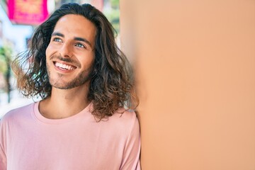 Young hispanic man smiling happy looking to the side leaning on the wall