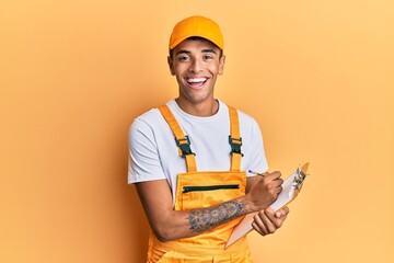 Poster - Young handsome african american man wearing courier uniform holding clipboard smiling and laughing hard out loud because funny crazy joke.