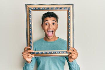 Poster - Young handsome african american man holding blank empty banner celebrating crazy and amazed for success with open eyes screaming excited.