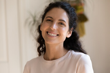 Adorable millennial female posing for headshot portrait smiling looking at camera. Profile picture of happy young woman with shiny smile making video call from home taking part in virtual conference