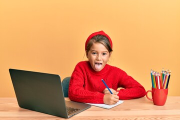 Wall Mural - Little beautiful girl studying using computer laptop sticking tongue out happy with funny expression.