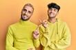© Krakenimages.com - Homosexual gay couple standing together wearing yellow clothes with a big smile on face, pointing with hand and finger to the side looking at the camera.