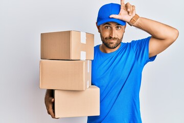 Wall Mural - Handsome man with beard wearing courier uniform holding delivery packages making fun of people with fingers on forehead doing loser gesture mocking and insulting.