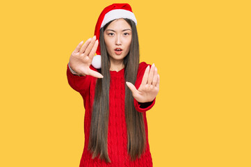 Sticker - Young chinese woman wearing christmas hat doing stop gesture with hands palms, angry and frustration expression