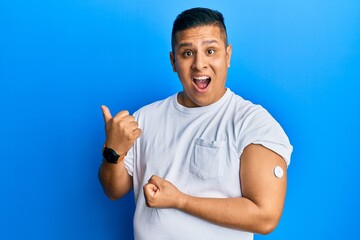 Canvas Print - Young latin man using glucose meter button pointing thumb up to the side smiling happy with open mouth