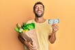 © Krakenimages.com - Handsome man with beard holding groceries and 1 american dollar banknote smiling and laughing hard out loud because funny crazy joke.