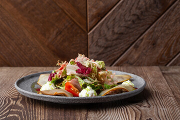 A tasty salad with pear, tomato, mozzarella cheese and fresh lettuce, dressed with a red and green sauces. Side close-up on a grey round plate on a wooden background with copy space. Healthy food.