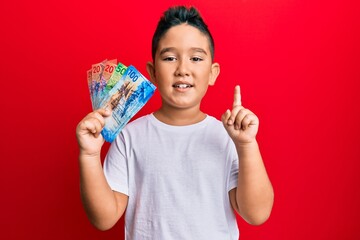 Canvas Print - Little boy hispanic kid holding swiss franc banknotes smiling with an idea or question pointing finger with happy face, number one