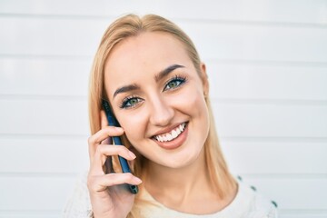 Young blonde girl smiling happy talking on the smartphone at the city.