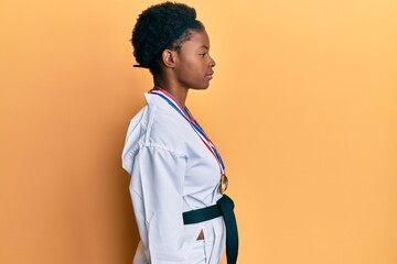 Poster - Young african american girl wearing karate kimono and black belt looking to side, relax profile pose with natural face with confident smile.