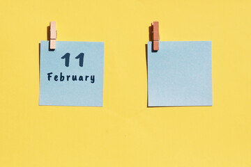 11st of February. 11st day of the month, calendar date. Two blue sheets for writing on a yellow background. Top view, copy space. Winter month, day of the year concept