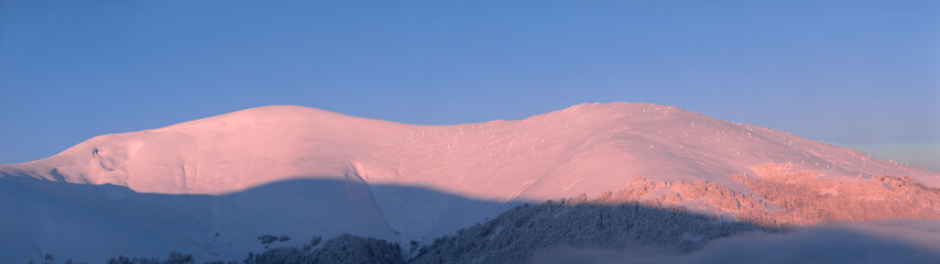 Mountain landscape. Snow-capped mountain peaks and fog at dawn.