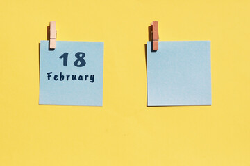 18st of February. 18st day of the month, calendar date. Two blue sheets for writing on a yellow background. Top view, copy space. Winter month, day of the year concept