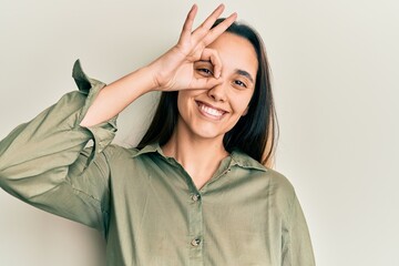 Poster - Young hispanic woman wearing casual clothes smiling happy doing ok sign with hand on eye looking through fingers