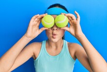 Beautiful Brunette Little Girl Holding Tennis Ball Close To Eyes Making Fish Face With Mouth And Squinting Eyes, Crazy And Comical.