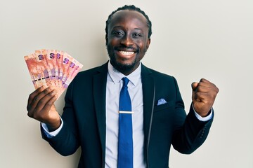 Canvas Print - Handsome young black man holding south african rand banknotes screaming proud, celebrating victory and success very excited with raised arm