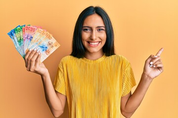 Wall Mural - Young brunette woman holding swiss franc banknotes smiling happy pointing with hand and finger to the side