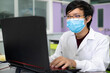 © bung - Front view of Young Asia scientist wear protective hygiene mask and using laptop in the modern laboratory. Research and education concept. Typing the keyboard and finding information online