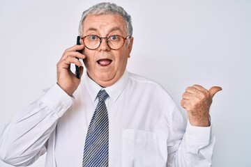 Sticker - Senior grey-haired man wearing business clothes having conversation talking on the smartphone pointing thumb up to the side smiling happy with open mouth