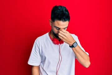 Wall Mural - Young man with beard listening to music using headphones tired rubbing nose and eyes feeling fatigue and headache. stress and frustration concept.