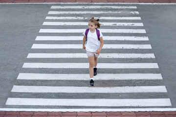 Schoolgirl crossing road on way to school. Zebra traffic walk way in the city. Concept pedestrians passing a crosswalk.  Stylish young teen girl walking with backpack. Active child. Top view