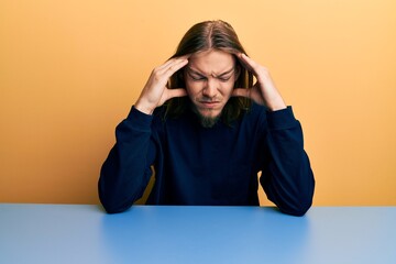 Wall Mural - Handsome caucasian man with long hair wearing casual clothes sitting on the table suffering from headache desperate and stressed because pain and migraine. hands on head.