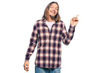 Handsome caucasian man with long hair wearing hipster shirt with a big smile on face, pointing with hand and finger to the side looking at the camera.