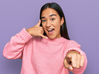 Canvas Print - Young asian woman wearing casual winter sweater smiling doing talking on the telephone gesture and pointing to you. call me.