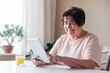 © sergign - An elderly woman uses a tablet at home and watches content on social networks - An elderly person knows how to use modern technologies .