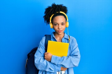 Wall Mural - Young african american girl wearing student backpack and headphones holding book skeptic and nervous, frowning upset because of problem. negative person.