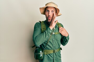 Canvas Print - Handsome man with beard wearing explorer hat and backpack hand on mouth telling secret rumor, whispering malicious talk conversation